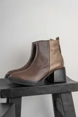 Bota corta de cuero marrón con puntera redondeada y taco cuadrado. Presenta una correa con hebilla alrededor del tobillo y cierre lateral.