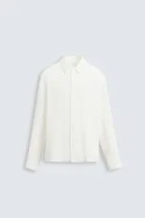 Camisa de hombre de corte relajado, color blanco, con textura plisada o acanalada vertical y manga larga con puño abotonado.