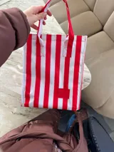 Bolso tipo shopper de tela blanca con rayas verticales rojas y asas rojas.