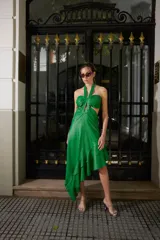 Vestido verde brillante, con escote halter anudado al cuello, aberturas laterales (cut-outs) y falda asimétrica con volados en el ruedo.