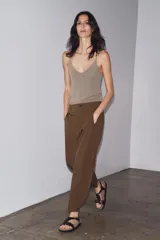 Pantalón marrón de tiro medio con trabillas en la cintura, bolsillos laterales, pinzas delanteras y bajo ajustable con trabilla y botón.