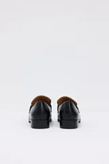 Mocasín negro de cuero liso, con punta cuadrada y hebilla metálica plateada en el empeine. Posee un taco bajo y cuadrado.