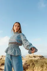 Blusa blanca de manga larga con cuello alto fruncido y detalle de smock en puños y cintura. Estampado floral en tono azul suave.