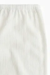 Pantalón recto color crema, de tejido arrugado suave, con cintura elástica y cordón ajustable.
