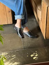 Mules de cuero color marrón con punta cuadrada y detalle de tachas doradas.