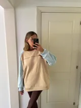 Buzo color beige con mangas celeste pastel y puños y ruedo acanalados.