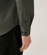 Camisa verde militar de manga larga en sarga de algodón, con cuello clásico, cierre frontal abotonado y dos bolsillos con solapa abotonada en el pecho.