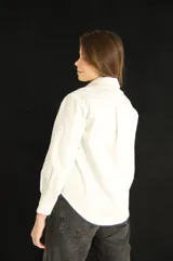 Camisa blanca de corte clásico con bolsillo en el pecho, mangas largas y botones al tono.