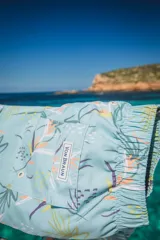 Short de baño celeste con estampado de hojas y flores en tonos naranja, verde y gris. Tiene elástico en la cintura, tres bolsillos y logo de la marca en la parte trasera.