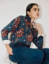 Buzo de tejido de punto azul marino con estampado floral en tonos terracota y verde azulado. Presenta cuello alto con cierre parcial frontal y puños y ruedo acanalados.