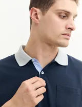 Remera polo blanca de piqué con cuello y puños en azul marino. Tiene tapeta de dos botones y bolsillo de parche en el pecho.