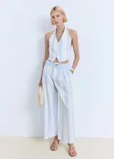 Top tipo chaleco con cuello halter y cierre frontal de tres botones. Presenta un diseño entallado con rayas verticales celestes y blancas, dos bolsillos frontales de ribete y ajuste de hebilla en la espalda.