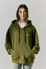 Buzo verde militar de algodón rústico con capucha, corte oversize, cierre metálico, bolsillos delanteros, estampa en frente y espalda, cordón con puntera de goma y lavado acid wash suave.