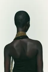 Top negro con cuello halter, escote pico y espalda descubierta. Presenta detalle de frunces laterales y cierre frontal con botones.