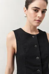 Chaleco sastrero negro sin mangas, con cuello redondo, botones metálicos frontales a presión y bolsillos ojal en la parte inferior.