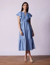 Vestido midi celeste de tencel con cuello a la base y escote en V. Cintura con frunces y lazo de ajuste. Terminación de ruedo con volado.