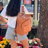 Mochila de eco-cuero color marrón, con múltiples bolsillos frontales y laterales, y asa superior.