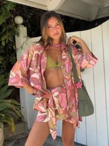 Falda pareo corta con estampado floral grande en tonos rosados, naranjas y beige. Se anuda al costado y tiene un corte asimétrico.