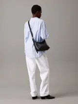 Bolso de hombro o cruzado de piel sintética negra, de forma rectangular y suave, con cierre superior de cremallera y correa ajustable con herrajes metálicos.