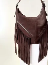 Bolso tipo hobo color tostado, hecho de cuero con flecos largos en el frente y dos bolsillos con cierre. Tiene una manija regulable con hebillas metálicas.