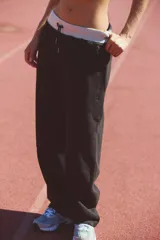 Pantalón de tela oscura, posiblemente negro o gris oscuro, con corte ancho y holgado (barrel). Presenta un elástico de cintura ancho y acanalado en color gris claro/blanco con cordón ajustable.