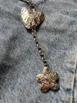 Collar metálico plateado con dije de corazón y de flor. La cadena está formada por dos modelos distintos: una con caritas sonrientes y otra de eslabones.