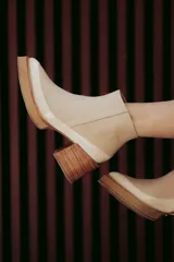 Bota de cuero negro con detalle en charol y taco ancho de madera natural, diseño minimalista.