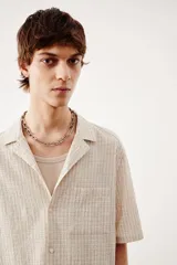 Camisa de manga corta color crema en tejido sirsaca de algodón. Modelo boxy con cuello abierto, tapeta lisa, bolsillo superior y bajo recto. Corte holgado.
