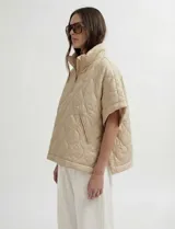 Poncho acolchado color mostaza con cuello alto y abertura frontal con cierre. Presenta un patrón capitoné de formas ovaladas y bolsillos delanteros.