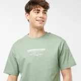 Camiseta verde con estampado rectangular en el pecho con texto en blanco.