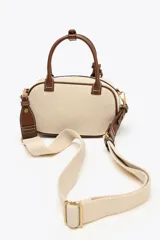 Bolso mini color crudo con detalles en marrón. Tiene asa de mano y doble asa bandolera extraíble, una en tejido tipo canvas y otra con pespunte. Incluye charm con piezas metálicas y bolsillo interior con cremallera.