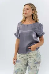 Blusa gris lavanda metálico de corte recto y fluido, con mangas cortas con vuelta, escote redondo y abertura en la espalda.