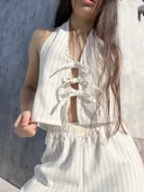 Top halter color beige con rayas verticales blancas y lazos ajustables en el frente y en la espalda.