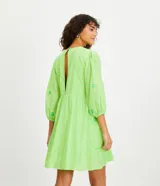 Vestido corto color verde lima con estampado de flores en verde claro, escote en V con lazo, mangas 3/4 con puños elásticos y falda con volantes.