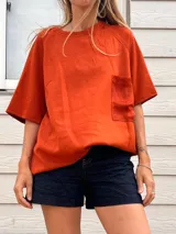 Remera holgada color naranja quemado, con cuello redondo y mangas raglán cortas. Posee un bolsillo de parche en el pecho, aparentemente de un material diferente o con textura contrastante.