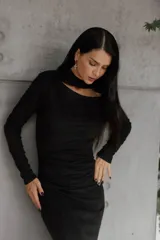 Vestido negro de largo midi, confeccionado en tejido grueso con efecto ante. Presenta mangas largas, escote con abertura en el pecho, cintura elastizada con frunces, tajo lateral y cuello medio alto.