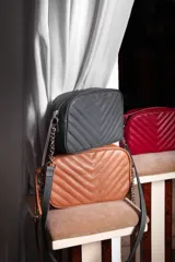 Cartera bandolera negra con diseño capitoneado en forma de V, correa de cuero y cadena plateada, cierre metálico y doble bolsillo interior.