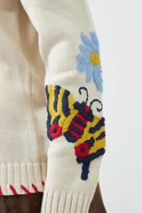 Cárdigan color crema con botones, ribete rojo y bordados de flores y mariposas en las mangas.