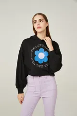 Buzo negro cropped con capucha y mangas largas abullonadas. Estampado frontal con una flor azul y texto en blanco.