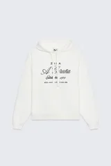 Sudadera blanca de algodón con capucha ajustable con cordones y mangas largas. Presenta un bordado negro con la inscripción "Zara A Coruña Establecida 1975 Rúa Juan Flórez 64-66" en el frente. Terminaciones en rib.