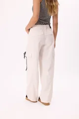 Pantalón cargo color crudo, de denim liviano, con tiro medio, pierna amplia y bolsillos laterales. Incluye tiritas trenzadas con pañuelo estampado atadas a la cintura.