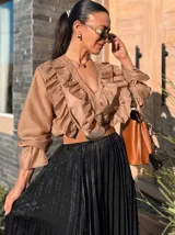 Camisa o blusa de organza color beige, con amplios volados en el frente y escote en V. Presenta mangas largas con puños fruncidos.