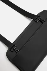 Bandolera negra con acabado engomado, compartimento principal con cierre de cremallera y bolsillo interior con cremallera. Asa de hombro ajustable y extraíble.