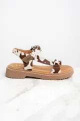Sandalias con estampado animal print de vaca, con suela marrón y hebilla ajustable.