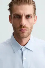 Camisa negra de manga larga con cuello italiano y cierre frontal de botonadura. Presenta un tejido con estructura de fácil cuidado.