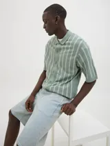 Polo de punto verde con rayas verticales blancas, corte relajado, cuello tipo camisa, cierre con botones y mangas cortas.