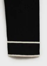Jersey de punto fino color negro con cuello de pico y ribetes en contraste blanco en el cuello y puños. Diseño recto y manga larga.