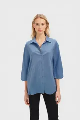 Camisa celeste de corte holgado con cuello clásico, cierre frontal con botones y mangas 3/4 con puños.