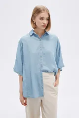 Camisa celeste de manga corta, corte holgado, con cuello camisero y cierre frontal con botones.
