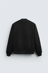 Cazadora bomber negra de corte regular, confeccionada en tejido con efecto ante. Cuenta con cuello, puños y bajo de rib elástico, bolsillos de vivo en la cadera y cierre frontal con cremallera.